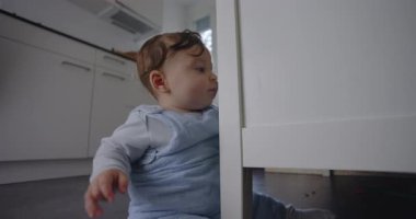 Bebek mutfak zemininde oturmuş, aile ortamının erken gelişimi sırasında merak ve bağımsızlığını gösteriyor.