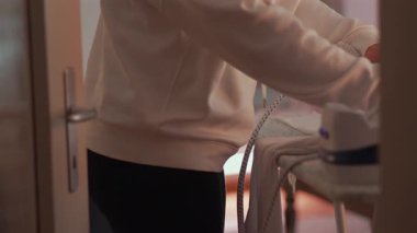 Evdeki kıyafetleri ütüleyen kadın, odaklanma ve rutin bakımda kumaşı dikkatlice düzelten eller, ev hayatının sembolü ve sessiz günlük sorumluluğun.