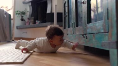 Bebek yerde yatıp mobilyaların altına bakıyor. Sıcak ev ortamının gelişimi sırasında erken keşif ve büyülenmeyi gösteren ilginç bir an.