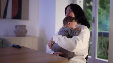 Anne, akşam evde ağlayan bebeği sakinleştirmeye çalışırken kendini çok yorgun hissediyor, ebeveynlik yorgunluğu ve duygusal baskı gösteriyor.