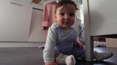 Bebek mutfak zemininde yatarken, evde keşif ve farkındalığın erken safhalarında odak ve sessiz bir gözlem sergileyerek çevreye tuhaf bir şekilde bakıyor.