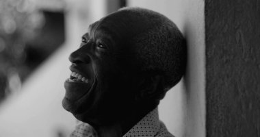 Siyah beyaz bir duvara yaslanmış, neşe, pozitiflik ve duygusal derinlik aktaran Afrikalı Amerikalı yaşlı bir adam gülüyor.