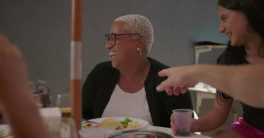 Bir grup arkadaş açık hava yemek masasında birlikte gülüyor ve eğleniyorlar, çeşitli etnik köken ve doğal, otantik neşe sergiliyorlar.