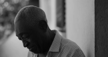 Siyah beyaz bir duvara yaslanmış, neşeyle gülen Afrikalı Amerikalı yaşlı bir adam, mutluluk, memnuniyet ve duygusal sıcaklık saçan, siyah beyaz bir şekilde yakalandı.