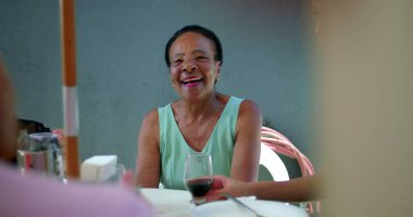 Yaşlı bir kadın açık havada bir aile yemeği sırasında gülüyor ve canlı bir sohbete dalıyor, canlı ve neşeli bir etkileşim kuruyor, gelişigüzel bir ortamda çoklu nesiller arası bağ kuruyor.