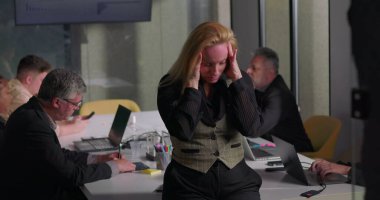 Ofis toplantısı sırasında gergin bir ifadeyle el ele tutuşan sarışın iş kadını, takım konferans masasında çalışırken baskı altında kalıyor.