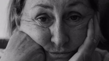 Nazik bir ifadeyle yüzünü dinlendiren yaşlı bir kadının yakın plan portresi, düşünceli ve dikkatli bir bakış, siyah ve beyaz olarak sessiz bir merak ve duygusal derinlik aktarıyor.