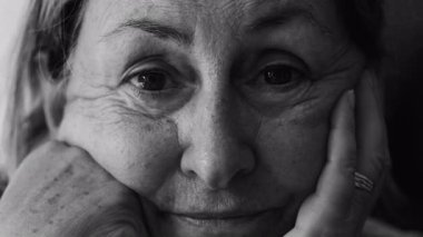 Yüzü ellerinde dinlenen yaşlı bir kadının yakın plan portresi, doğrudan bakışlarla sakin iç gözlem ve duygusal sıcaklığı gösteren nazik bir ifade, siyah ve beyaz.