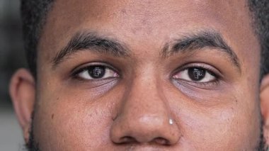 Genç siyah adamın burun delici gözleri, sakin ve tarafsız bir ifadeyle kameraya sessizce bakıyor.