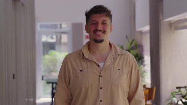 Genç adam sakince kameraya gülümsüyor, doğal bir portre arkadaşlığı, açıklığı ve ev ortamında kendine güveni ifade ediyor..