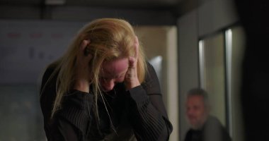 Sarışın iş kadını ofiste duygusal sıkıntılarla boğuşuyor. Yoğun takım toplantısı sırasında baş ve yumruklarını sıkıyor.