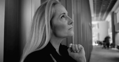 Geniş koridorda duvarın önünde dikilirken ve ofis mobilyaları yumuşak odak noktasında duran siyah beyaz kadın görüntüsü