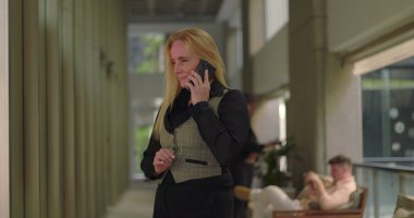 İş kadını, ofis koridorunda telefonla konuşurken, gayri resmi konuşma sırasında gülümsüyor ve yürüyor.