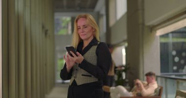 İş kadını, ofis koridorunda telefonla konuşurken, gayri resmi konuşma sırasında gülümsüyor ve yürüyor.