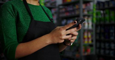 Hırdavatçı, bir hırdavatçıda akıllı telefondan mesajları yönetir, birden fazla mesleki görev ve iş iletişimine dikkat gösterir.