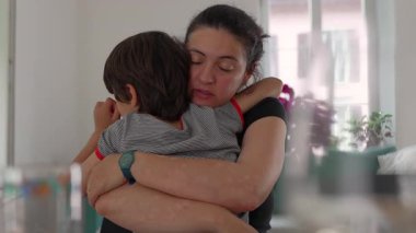 Anne çocuğu gözleri kapalı kucaklıyor, sıcak bir yuva kurarken derin şefkat ve güven gösteriyor.