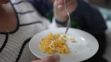 Tabaktaki çırpılmış yumurtaları yakından izleyin. Kadın tabağı tutar ve tek eliyle yer. Basit bir yemek sırasında.