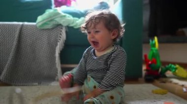 Bir çocuğun plastik bir kabı fırlatıp tekrar ona doğru emeklediği, rahat bir ev ortamında merak, hareket ve erken keşifler yaptığı neşeli bir an..