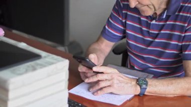 Kişisel cep telefonu etkileşiminin sakin anı sırasında ofis masasında otururken odaklanmış bakışlı akıllı telefon tutan kıdemli adam..