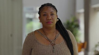 Afro-Amerikan kadın portresi. Tarafsız bir ifadeyle içeride duruyor. Sakin ve kendinden emin bir varlık.