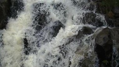 Hızla akan şelalenin karanlık kayaların üzerinden sıçraması, yüksek hızlı kamerayla akışkan hareket ve dokuyu yakalaması.