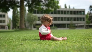 Şehir parkında çimenlerde sürünen çocuk, büyümeyi ve keşfi simgeleyen modern binalar ve ağaçlarla çevrili, azim ve merakla ileriye bakıyor.