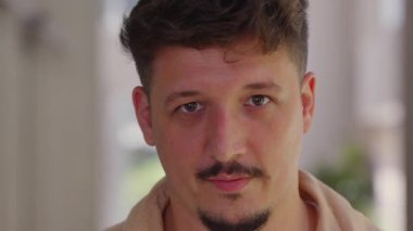 Sakin, nötr bir ifadeyle ileriye bakan genç bir adamın portresi, doğal ışıkta sakin bir güven ve varlığı iletiyor..