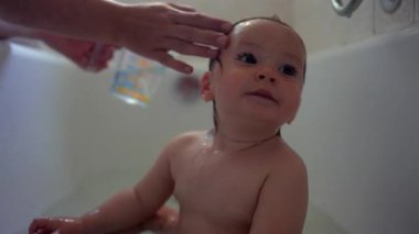 Bebek sıcak bir banyoda oturmuş, sakin ve tuhaf bir ifadeyle yukarı bakıyor. Su yüzünden akarken hassas bir an yaratıyor. Yumuşak duygular, masumiyet ve erken keşiflerle dolu.