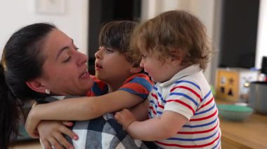 Anne, çocuklarını nazikçe kucaklıyor, kısa kardeş çatışmasından sonra duyguları yatıştırıyor, evde sevgi, sabır ve sakin bir bağ gösteriyor.