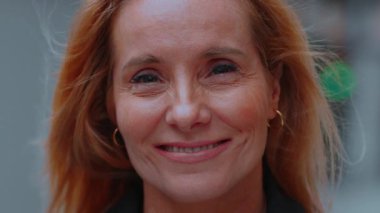 Açık havada gülümseyen orta yaşlı bir kadın, doğal ışıkla aydınlatılmış altın sarısı saçları, sıcaklığı, iyimserliği ve duygusal gerçekliği aktarıyor.