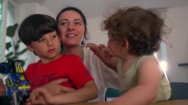 Anne neşeli bir şekilde ufaklıkların elini kullanarak ahududu üflerken, büyük kardeş eğlenceye katılıyor, kahkahalarla, şefkatle dolu sıcak bir aile anı yaratıyor ve neşeli bir enerjiyi paylaşıyor. 