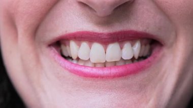 Dişi dudakların yakın çekimi. Hafif rujla gülümseyen, temiz bir kompozisyonda, yumuşaklığını ve zarafetini gösteren.