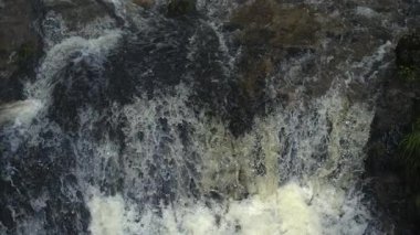 Köpüklü şelale suyunun yakın çekimi Ultra yavaş çekimde karanlık kaya yüzeyine çarpıyor. Yüksek hızlı bir kamerayla çekiliyor.