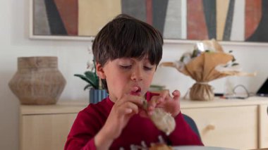 Bir çocuk tavuk butundan güçlü bir ısırık alır ve ev yapımı yemeğin tadını çıkarırken dramatik bir yemek ifadesi takınır..