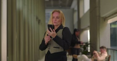 İş kadını, ofis koridorunda telefonla konuşurken, gayri resmi konuşma sırasında gülümsüyor ve yürüyor.