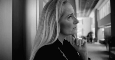 Geniş koridorda duvarın önünde dikilirken ve ofis mobilyaları yumuşak odak noktasında duran siyah beyaz kadın görüntüsü