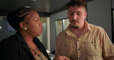 African American businesswoman explaining tablet data to young male colleague in office, active teamwork near conference table with charts on screen