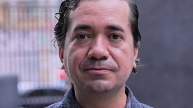 Orta yaşlı bir adam, sakin portre ayarında Tarafsız İfadesiyle doğrudan kameraya bakıyor.