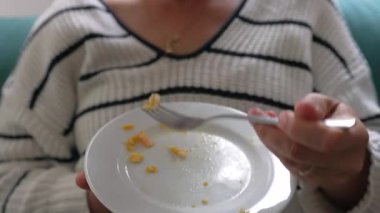 Kapalı alanda gevşetilmiş yemek sırasında elinde beyaz tabakla çırpılmış yumurta yiyen bir kadının yakın görüntüsü.