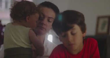 Annesi arka planda uyuyan bir bebeği tutarken genç bir çocuk sessizce oturur. Sakin ve sıcak bir duygu ve sıcak bir aile anı yaratır.