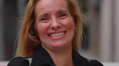 Orta yaşlı kadın açık havada gülümsüyor, neşeli ve kendinden emin portre sıcaklığı, özgünlüğü ve duygusal açıklığı yansıtıyor.