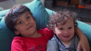 Büyük kardeş bebeğe sarılır ve yumuşak bir öpücük verir. Rahat bir yuva ortamında sıcaklıkla, şefkatle ve gerçek kardeşlikle dolu hassas bir an yaratır.