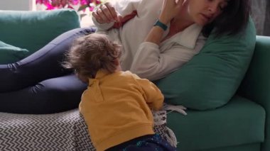 Anne kanepeye uzanıp küpelerini ayarlıyor. Yavaş ve sakin hareketlerle yeni yürümeye başlayan çocuk yakınlarda geziniyor. Her gün basit bir ebeveyn ve rahat bir ev hayatı kuruyor.