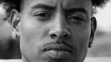 Ciddi bir ifadeyle genç Afrikalı Amerikalı adamın yakın plan portresi, çatık kaş kararlılık ve güç, güçlü erkeksi özellikler, siyah ve beyaz..