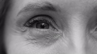 Orta yaşlı kadınların gözlerinin yakın plan portresi yumuşak ve yansıtıcı duygular, kirpiklerin ince dokusu ve derinin siyah ve beyaz olarak kendine olan güvenini ortaya koyuyor..