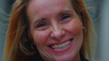 Orta yaşlı bir kadının yakın plan portresi gerçek neşe içinde gülümsüyor, gözleri kırışıyor ve dışarıya sıcaklık ve güven saçıyor.