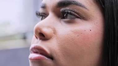 Düz saçlı, yansıtıcı gözlerle ve düşünceli ifadeyle mesafeye bakan genç bir kadının yakın portresi.