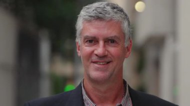 Açık havada beyaz saçlı orta yaşlı bir adamın gülümseyen portresi samimiyetini, samimiyetini ve samimiyetini ifade ediyor..