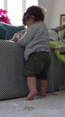 Bebek parmak uçlarında duruyor kanepeye yaslanıyor merakla odayı inceliyor, oyun etkileşimine odaklanıyor ve kapalı alanda erken gelişime odaklanıyor.