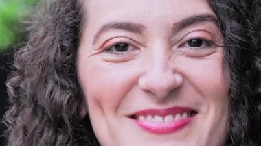 Açık renk makyajlı, koyu renk saçlı kadın kameraya sıcak ve kendinden emin bir ifadeyle gülümsüyor.